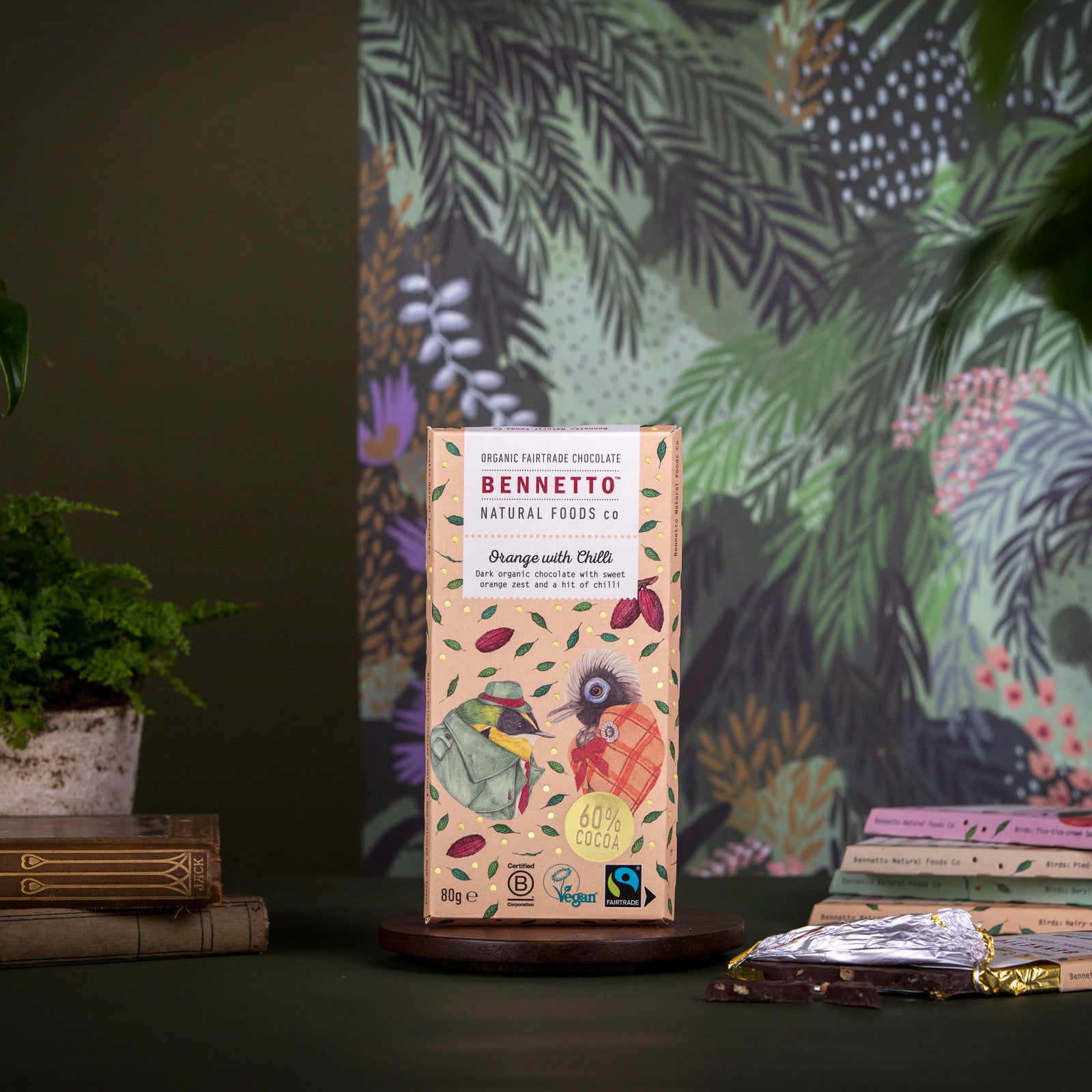 A bar of Bennetto Natural Foods organic, vegan and Fairtrade dark chocolate, Orange with Chilli flavour, on a beautifully decorated background with illustrations of birds and tropical plants.