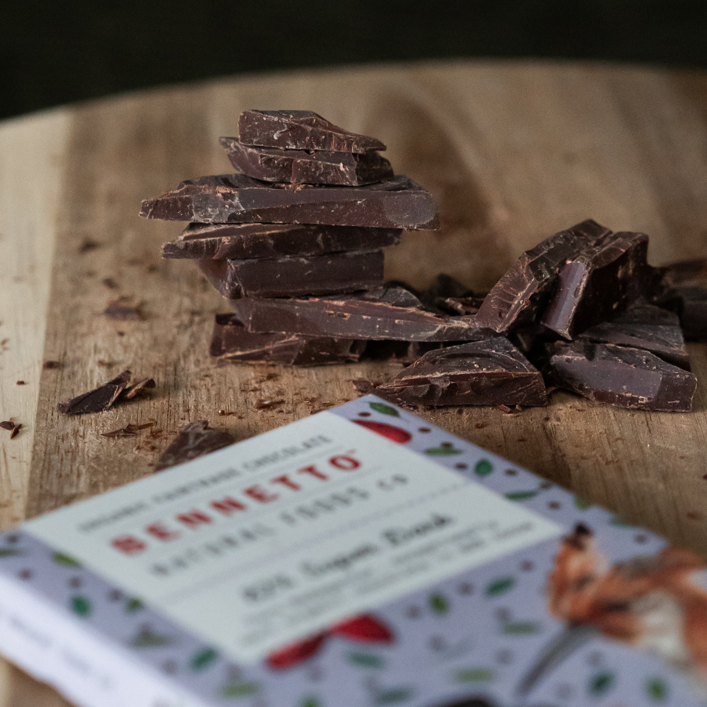 Stack of 82% Super Dark chocolate pieces on a wooden surface with a Bennetto bar in the foreground.