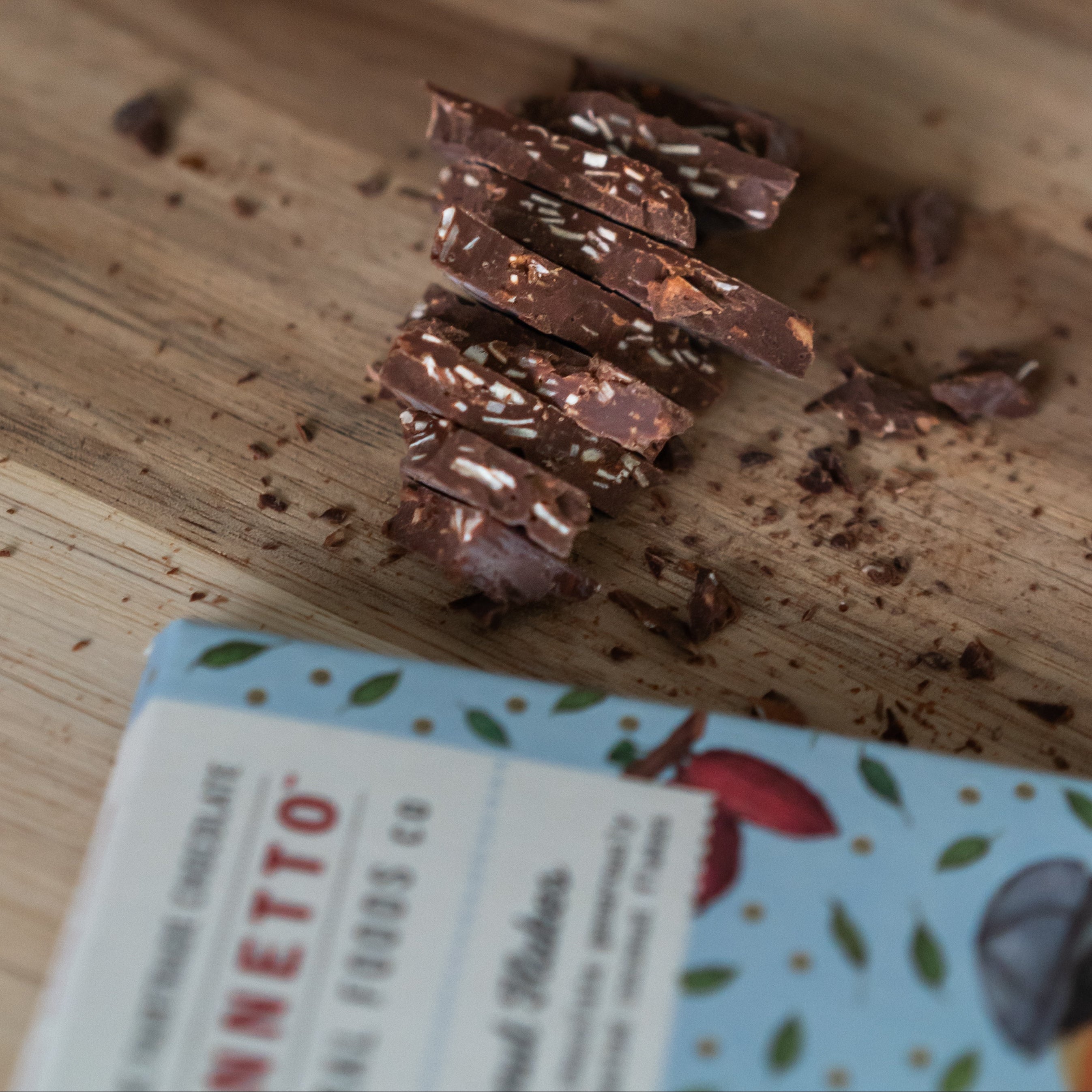 Bennetto Coconut Flakes organic dark chocolate pile on a brown table with bar lying in front