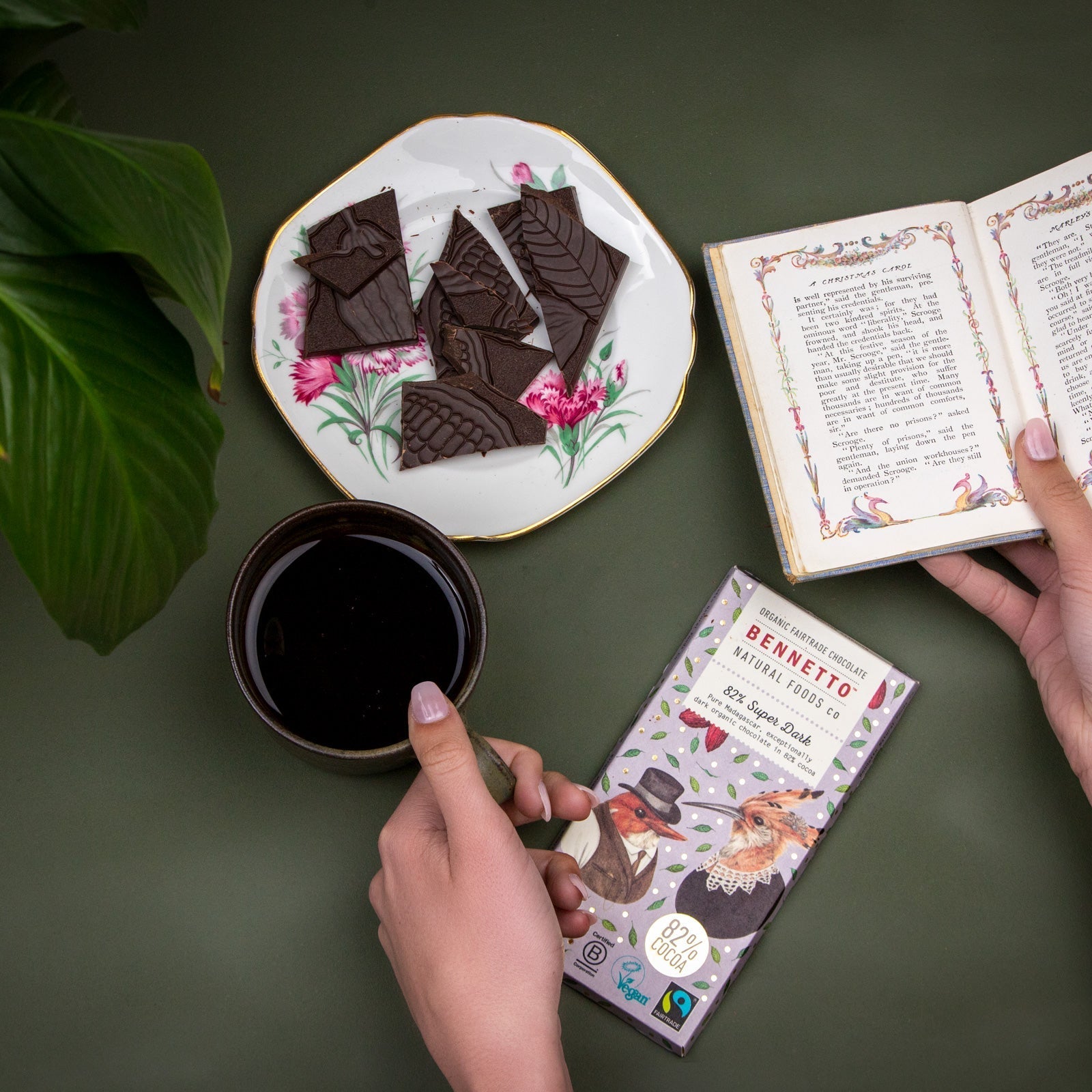 Someone reads and drinks tea while eating a bar of Bennetto 82% Super Dark organic & Fairtrade dark chocolate