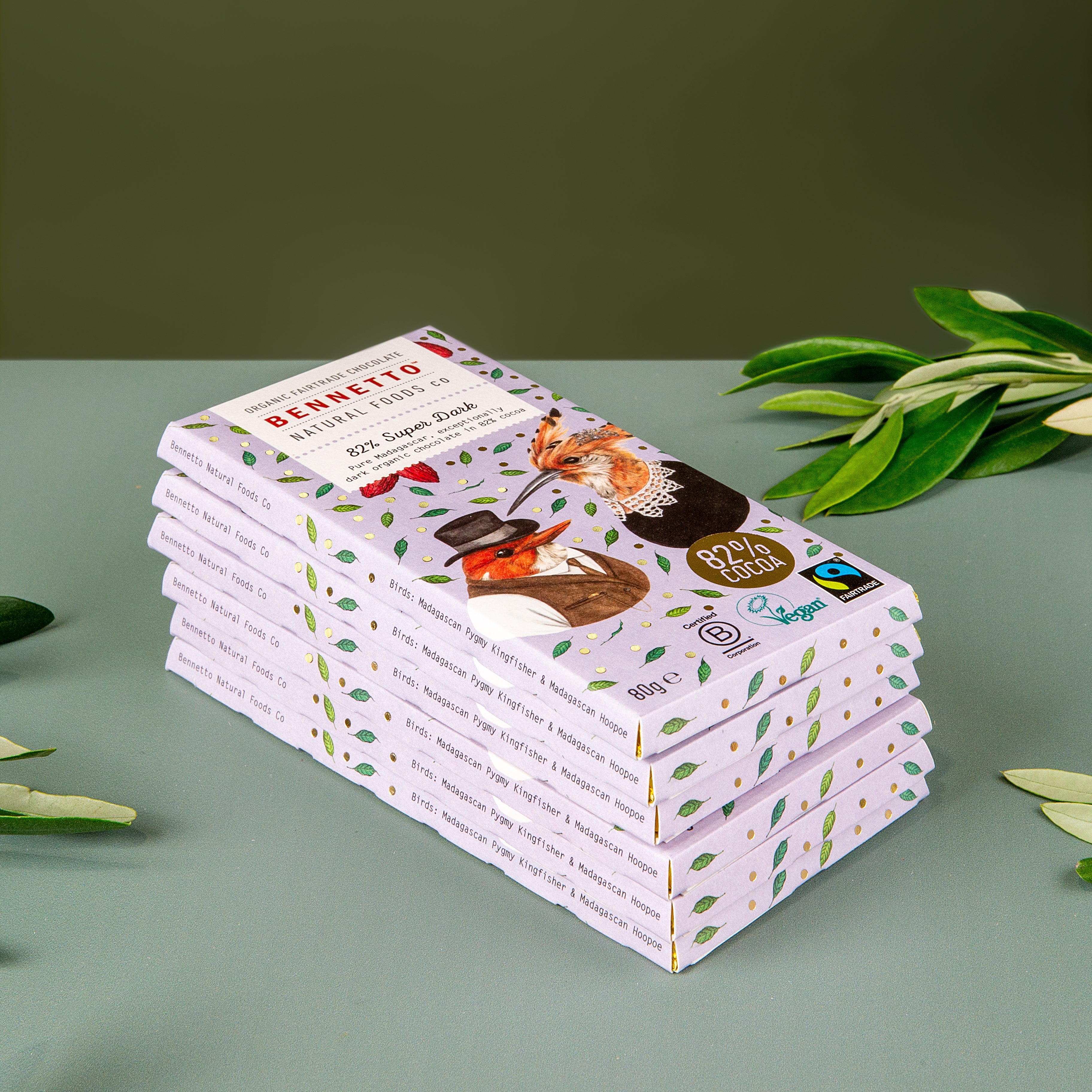 A stack of 6 bars of Bennetto 82% Super Dark Fairtrade and organic chocolate sits on a green table