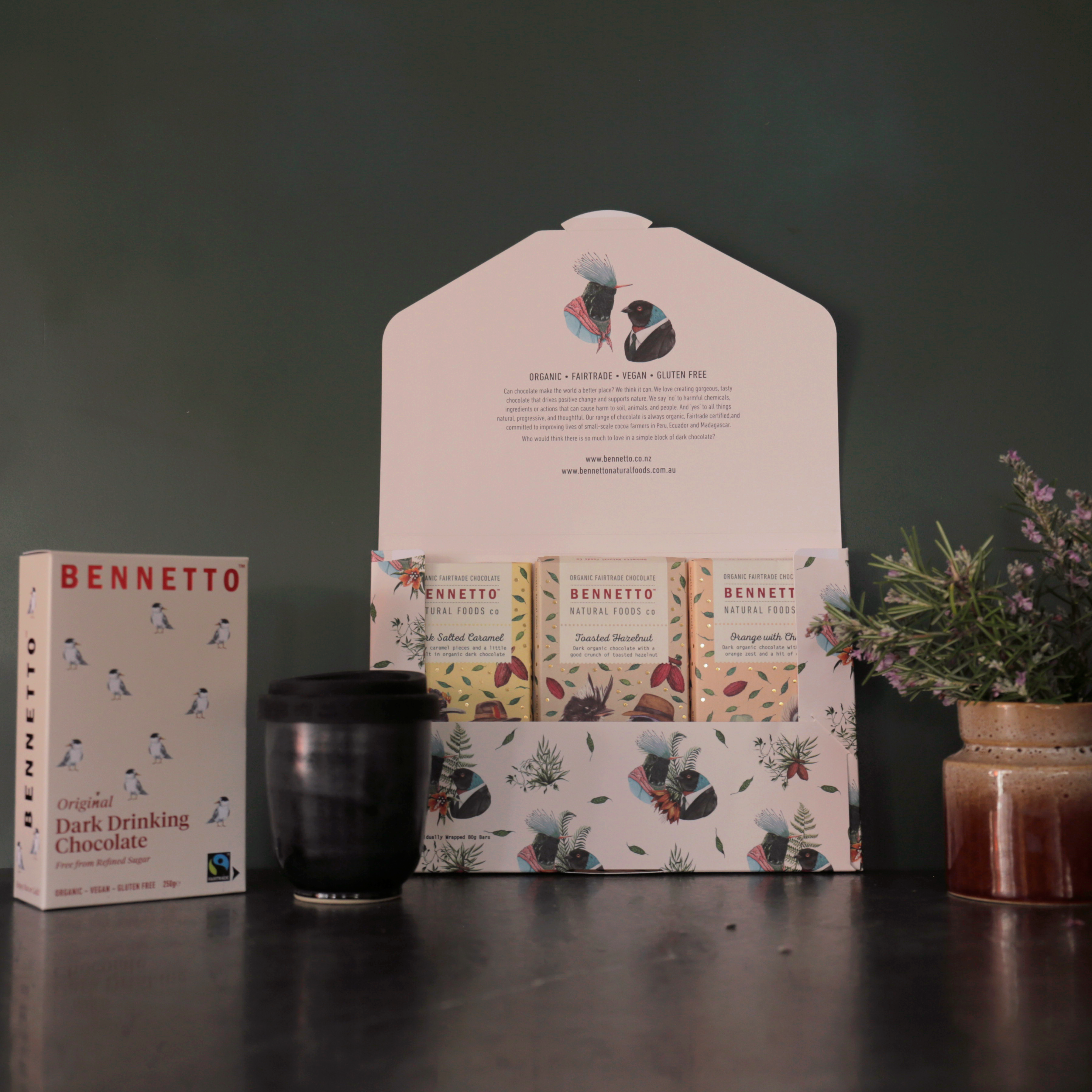 Bennetto chocolate bars and hot chocolate and a ceramic reusable travel mug on a dark surface with a green background