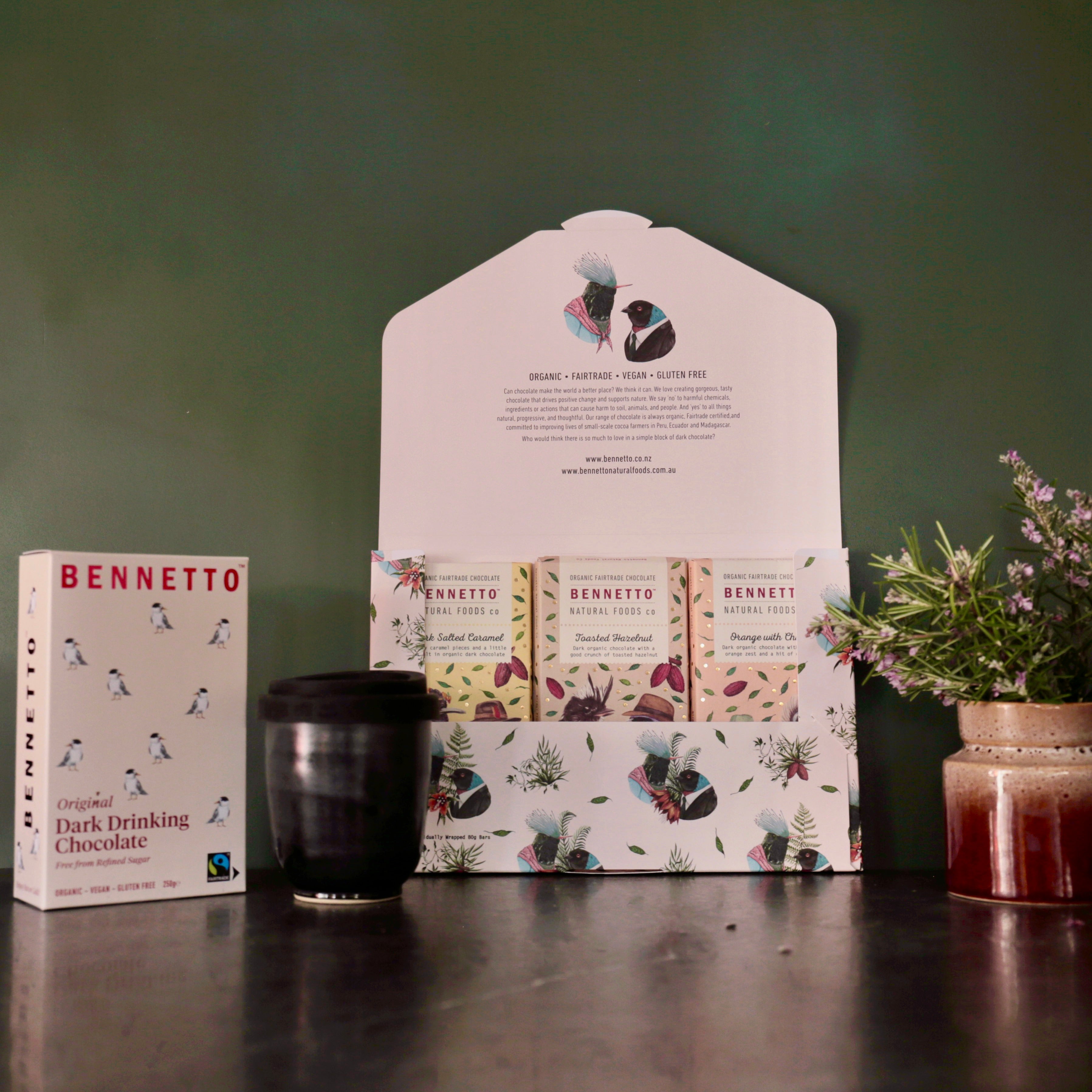 Bennetto gift pack containing 3 chocolate bars and hot chocolate and a ceramic reusable travel mug on a dark surface with a green background