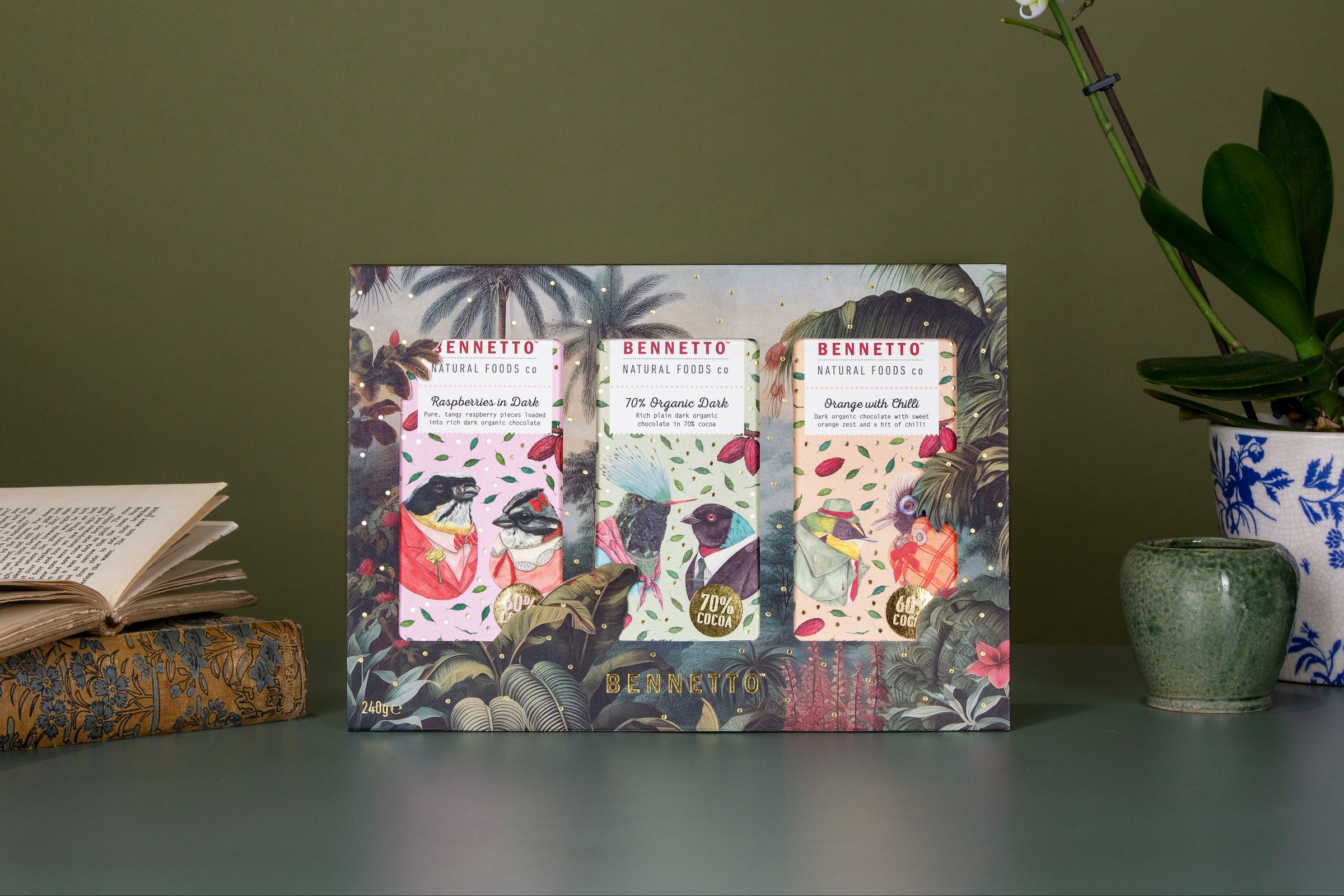 Fruit Jungle box including 3 x 80g bars Raspberries in dark, 70% organic dark, and Orange with chilli. aid in a pull out tray style packaging with watercolour jungle theme. Books to the left, orchid and plant pots to the right.