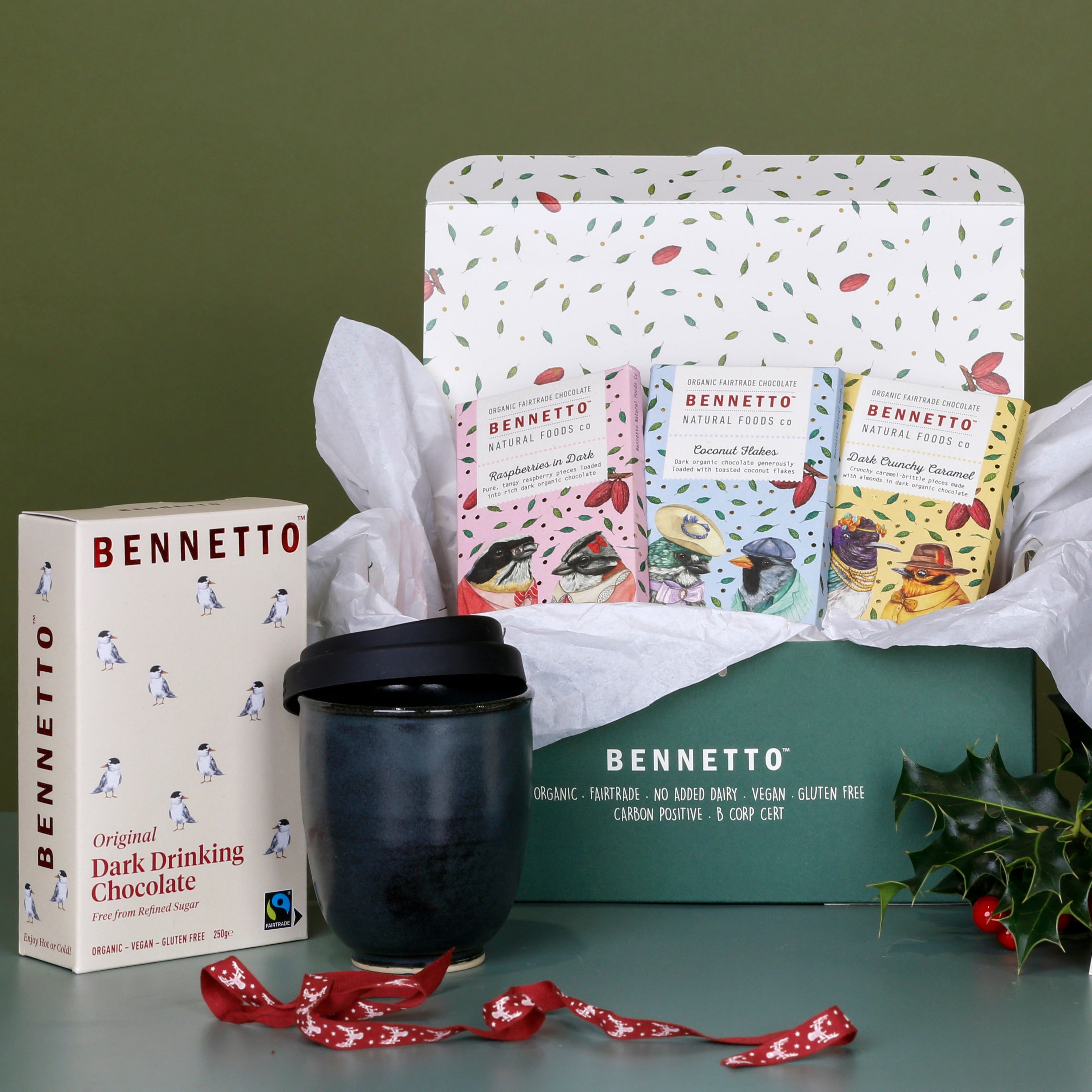 3 x Bennetto chocolate bars: Raspberries in Dark, Coconut Flakes, Dark Salted Caramel. In a green carton packaging, with tissue paper, a Bennetto Dark drinking Chocolate, with a handcrafted ceramic travel mug from the West Coast, on a green background with a Christmas theme.