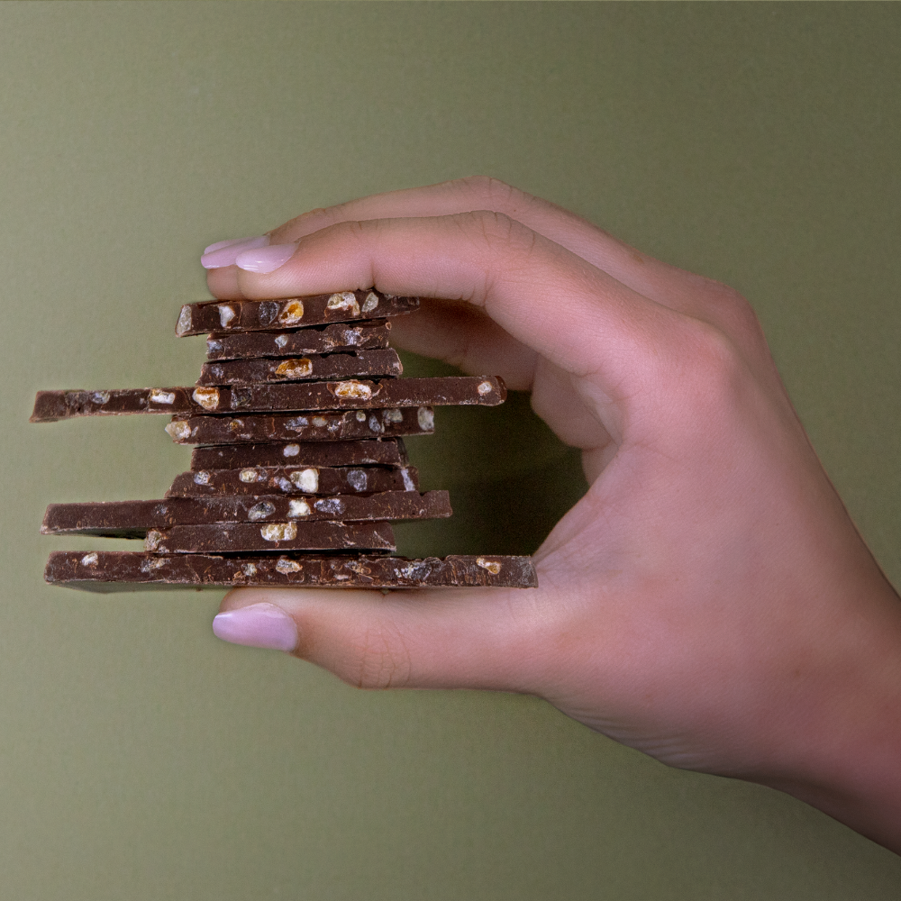Hand holding a stack of Bennetto Orange with Chilli organic and vegan dark chocolate pieces against a green background